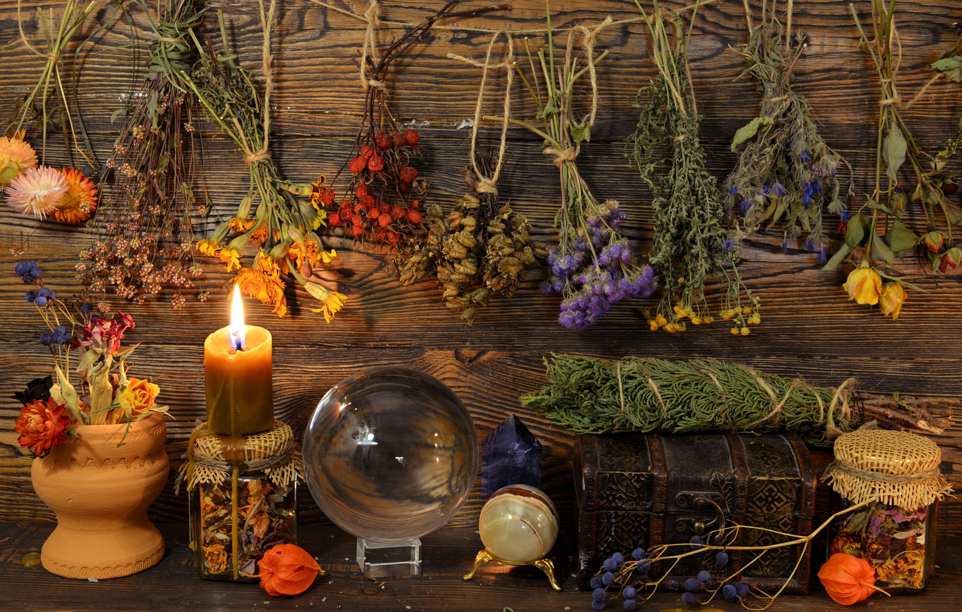 Still life with dry herbs, crystal ball, bottle and burning candle on witch table.